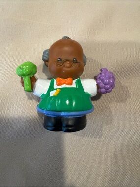 Fisher-Price Brown Shopkeeper Figure with Green Apron and Purple Grapes